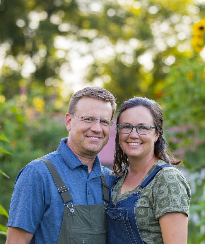 Jeremy and Staci Hill in overalls in their garden, with sunflowers behind them.